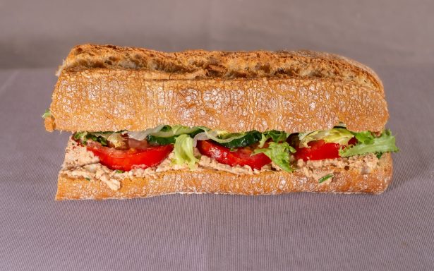 Sándwich de pan integral con lechuga, tomate y un untable cremoso.
